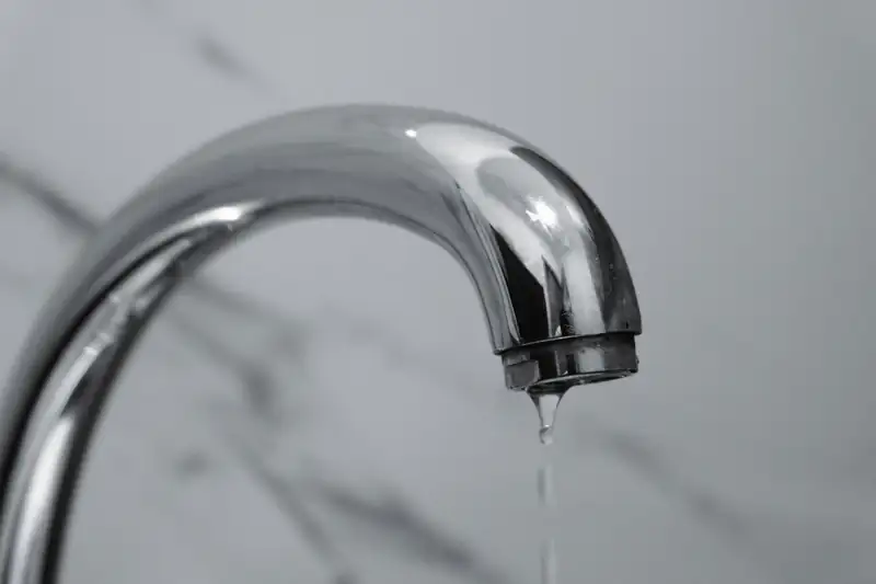 Close-up of a chrome bathroom faucet with a drop of water dripping from it
