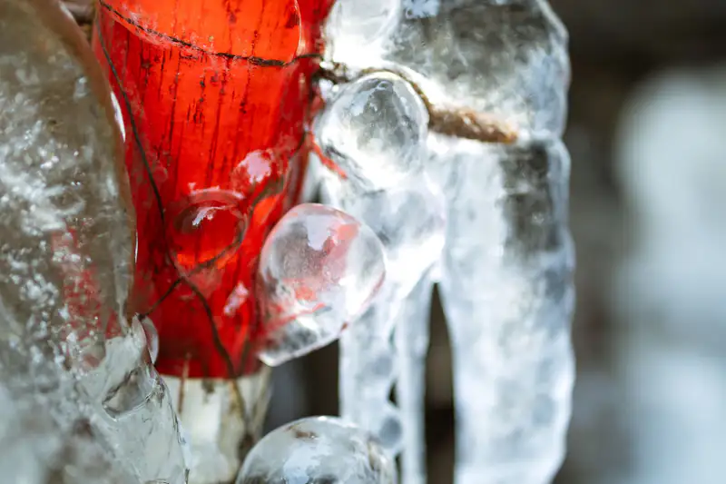 Ice and icicles forming on a red outdoor pipe in freezing weather