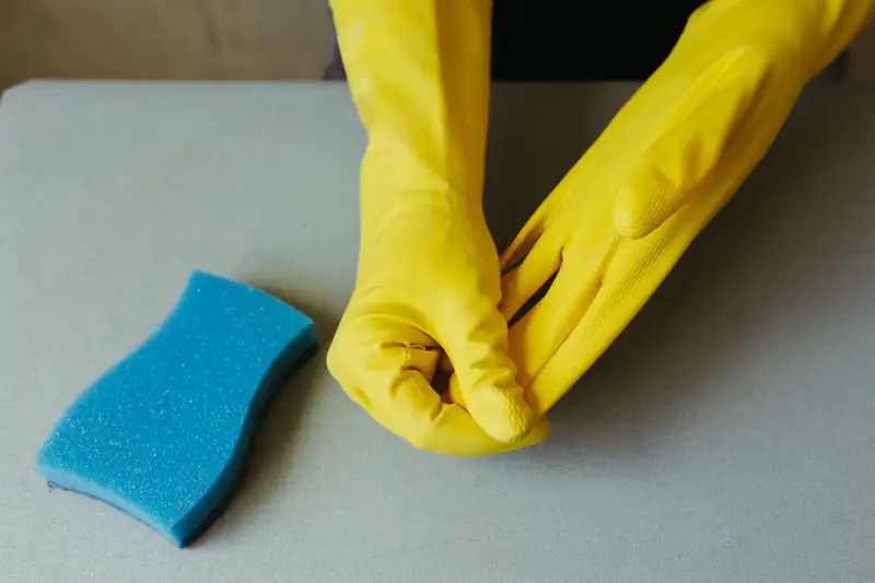 Hands in yellow rubber gloves next to a blue cleaning sponge