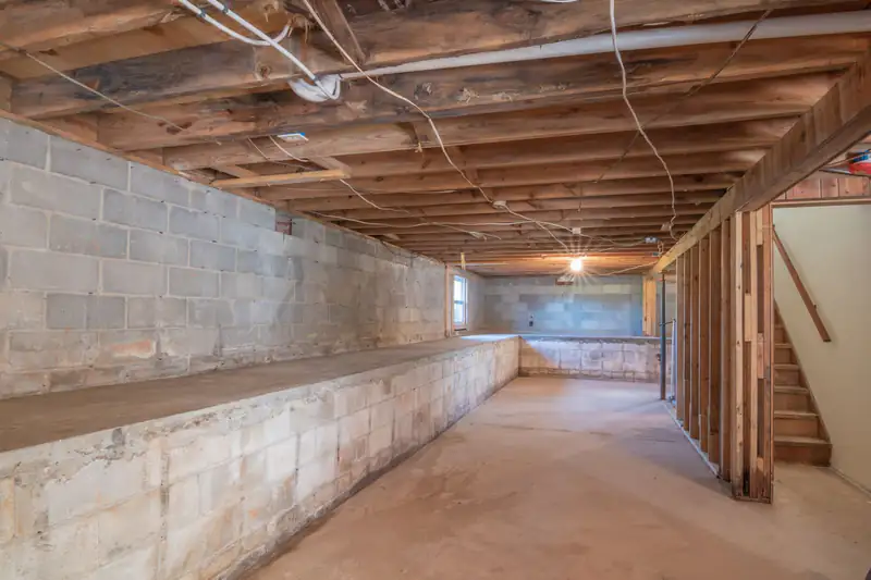 Unfinished basement with exposed wood joists, concrete walls and stairs